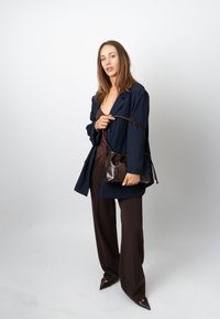 Sacou bleumarin peste un top maro, asortat cu pantaloni maro cu picior larg. O geantă mică, lucioasă, maro este ținută cu o curea de umăr.