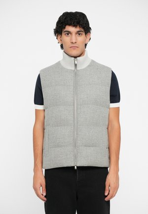 Vest puffer gri cu guler înalt, închidere cu fermoar și buzunare laterale; dispune de un material texturat cu un aspect matlasat. Puratat peste o cămașă bleumarin.