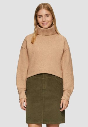 Beige, textuur, cropped coltrui met geribbelde manchetten, gecombineerd met een donkergroene corduroy rok. Beide kledingstukken hebben een eenvoudig design.