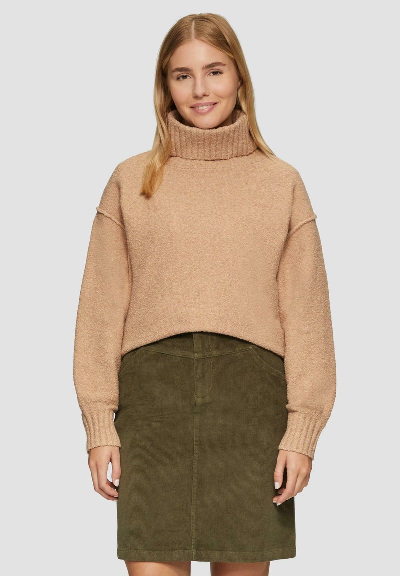 Beige, strukturierter, verkürzter Rollkragenpullover mit Rippabschlüssen, kombiniert mit einem dunkelgrünen Cordrock. Beide Kleidungsstücke zeichnen sich durch schlichte Designs aus.