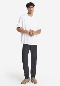 Vit t-shirt med korta ärmar kombinerad med mörka tajta jeans och ljusbruna sneakers. Enkel, avslappnad design utan synliga logotyper eller mönster.