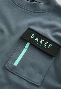 Szary sweter z czarną kieszenią, wyposażony w miętowozielony zamek i metkę z napisem "BAKER by TED BAKER". Gładka tekstura, fason z okrągłym dekoltem.