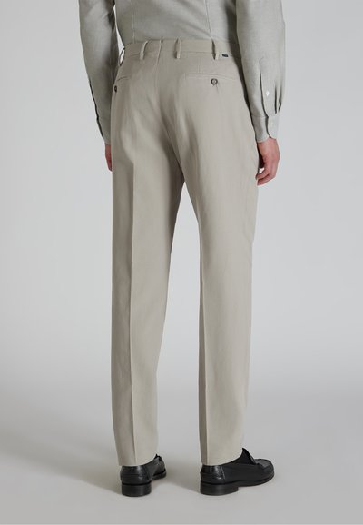 Pantalones beige claros de corte relajado. Presenta dos bolsillos traseros con cierres de botón. Combinados con zapatos negros. Tela suave y ligera.