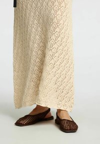 Brune net slingback flade sko med et åbent design, der har en rund tå og en flad sål, parret med en cremefarvet hæklede nederdel.
