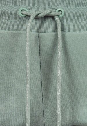 Groene sweatpants hebben een geribbelde tailleband met een trekkoord en gestikte accenten langs de beennaden, gemaakt van zachte, gestructureerde stof.
