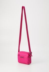Borsa a tracolla rosa di forma rettangolare, con un scomparto principale con zip, tasca frontale e tracolla regolabile con logo.
