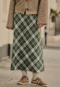 Grüner Karorock mit diagonalem Muster, kombiniert mit einer braunen, flauschigen Jacke, beigefarbenen und braunen Sneakern sowie beigen Socken.