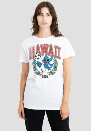 Junge Frau trägt ein weißes T-Shirt mit dem Schriftzug "HAWAII 2002" und einer blauen Cartoon-Figur, die vorne Fußball spielt.