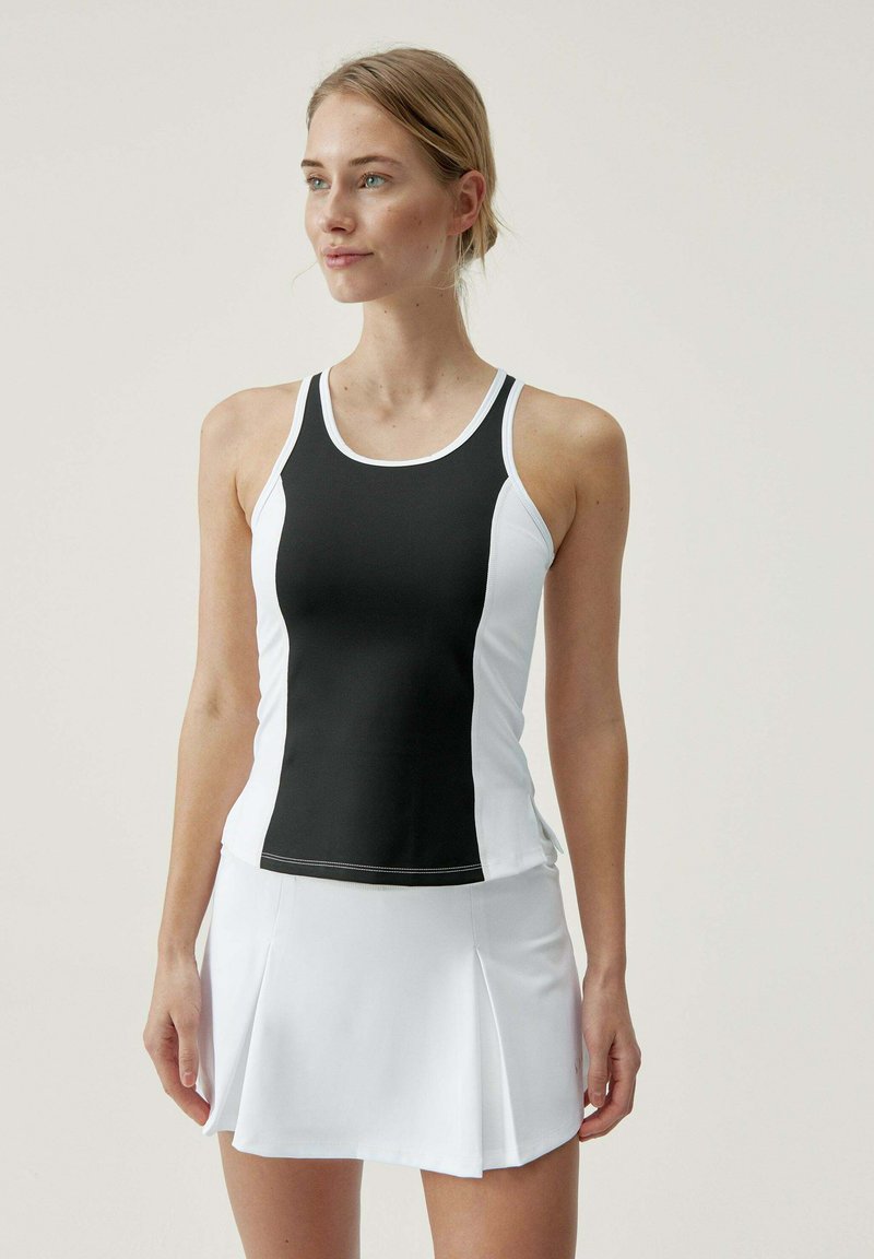 Top deportivo en blanco y negro con diseño de espalda nadadora y paneles laterales en contraste, combinado con una falda blanca plisada. Textura de tela suave.