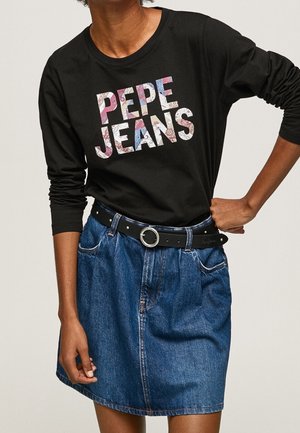 Osoba ubrana w czarną koszulkę z długim rękawem z kwiatowym napisem "PEPE JEANS" oraz niebieską dżinsową spódnicę z czarnym paskiem z okrągłą srebrną klamrą.