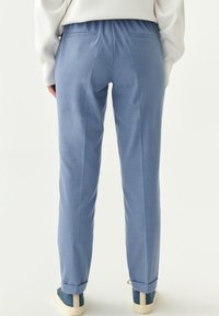Lichte blauwe, taps toelopende broek met een zachte textuur, een elastische tailleband en twee achterzakken. Bijgesneden enkels met contrasterende sneakers.