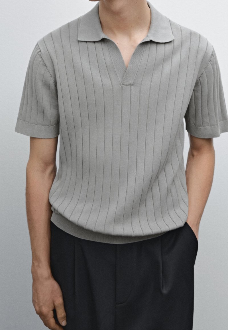 Short-sleeved, light gray knitted polo shirt with vertical stripes, collared neckline, and ribbed texture. Worn with dark trousers.