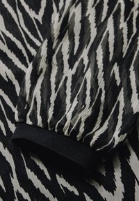 Tessuto a motivo zebra in bianco e nero con una finitura testurizzata. Presenta un polsino elastico nero arricciato e un design fluido.