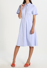 Ljusblå skjortklänning med vågkantat avslut och korta ärmar. I kombination med klarröda plattformssandaler. Mjuk tygtextur.