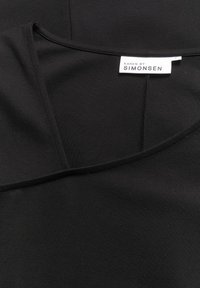 Musthave mustaga, millel on ümmargune kaelus ja sile tekstuur. Sildil on kirjas "KAREN BY SIMONSEN." Lihtne disain ja minimaalsed õmblused.