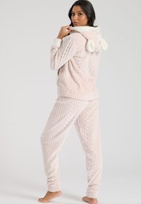 Conjunto de ropa de descanso de un suave color rosa claro, con un patrón de punto de cable texturizado, que incluye una capucha y detalles de pompón en la parte posterior de la chaqueta.