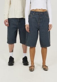 Bermudas de mezclilla en azul oscuro, con un corte relajado y bajos enrollados. Combinadas con zapatillas negras y zapatos planos con estampado.