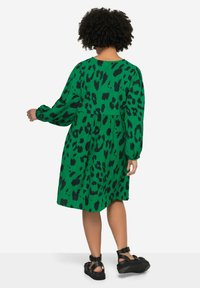 Groene jurk met een zwart panterprint, lange puffmouwen, een relaxte pasvorm en een verzamelde taille. Gepaard met zwarte sandalen.