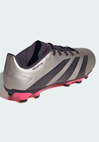 Botas de fútbol con una parte superior sintética gris elegante, acentos negros y una suela rosa. Cuenta con una superficie texturizada y cordones tradicionales.