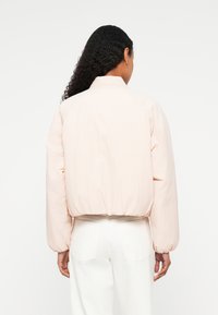 Veste bomber raccourcie rose clair avec des manches surdimensionnées, une taille cintrée et un col montant. Texture lisse et détails de design minimalistes.