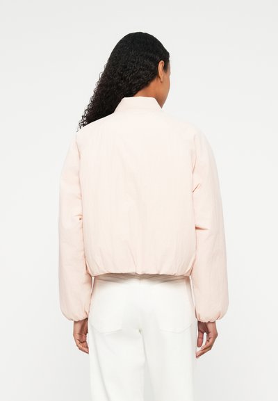 Veste bomber raccourcie rose clair avec des manches surdimensionnées, une taille cintrée et un col montant. Texture lisse et détails de design minimalistes.