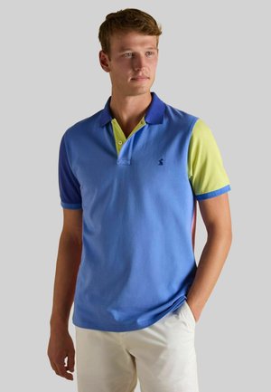 Polo shirt in blue cotton with short sleeves. Features a contrasting yellow collar and patterned accents in blue and green. Subtle logo on chest.