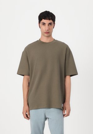 Olivengrøn ribbet kortærmet t-shirt med rund hals og afslappet pasform, parret med lyseblå denimjeans.