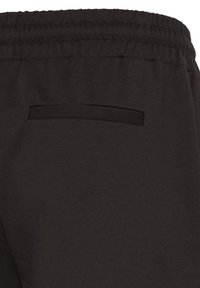 Black elastic waistband pants with a single horizontal back welt pocket, shown in close-up detail.