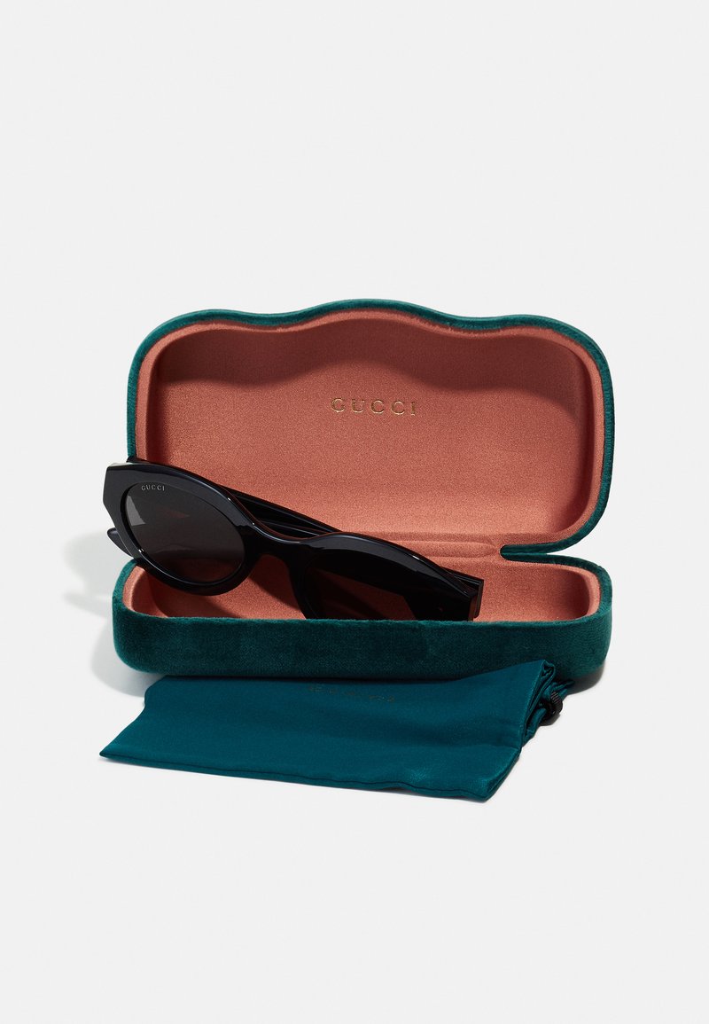 Black sunglasses in a green velvet case with a pink interior, featuring gold lettering. Includes a matching cleaning cloth.