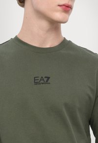 Zelené bavlnené tričko s okrúhlym výstrihom a krátkymi rukávmi, na hrudi vyšívané čierne logo EA7 Emporio Armani.