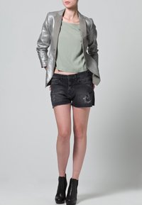 Blazer plateado metálico sobre una blusa verde clara, combinado con pantalones cortos de mezclilla negra desgastados y botas negras hasta el tobillo.