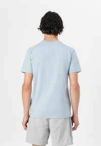 T-shirt bleu clair à manches courtes avec un col rond, fabriqué en coton doux. La vue de dos montre une texture lisse et un minimum de détails.