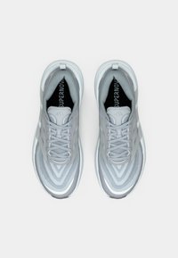 Chaussures de sport gris clair avec une tige texturée, un motif en zigzag et trois bandes blanches. Elles disposent d'une fermeture à lacets et d'une doublure intérieure douce.