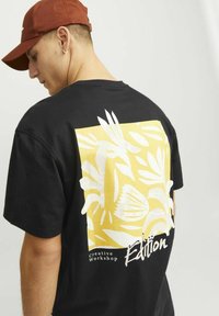 Čierne bavlnené tričko s veľkým grafickým dizajnom v žltej a bielej farbe na chrbte, s textom "Creative Workshop Edition."