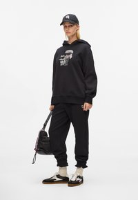 Felpa nera con cappuccio, decorata con un motivo grafico argento. Abbinata a pantaloni jogger neri, calze bianche e scarpe da ginnastica nere con un accento bianco.