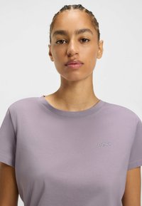 Lila t-paita lyhyillä hihoilla, pyöreällä kaula-aukolla ja brodeeratulla logolla rinnassa. Sujuva kangas, rento istuvuus.