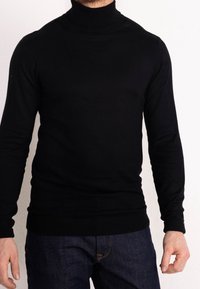 Czarny golf z długimi rękawami, dopasowany krój, wykonany z gładkiej tkaniny. Posiada prążkowany kołnierz i mankiety. Połączony z ciemnoniebieskimi dżinsami.