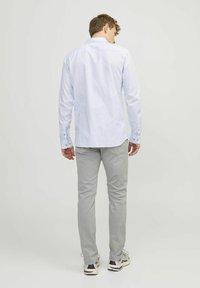 Světle modrá košile s knoflíky vyrobená z bavlny, se skladem na zádech, nošená s světle šedými kalhotami a teniskami, ukazuje neformální design.