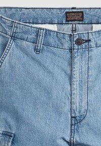 Svijetloplave traper šorts hlače s kopčanjem na gumbe, prednjim džepovima i vidljivim šavovima. Tkanina ima blago teksturiranu površinu.