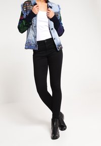 Jeansjacka med blommönstrade ärmar, ljusblå kropp och fransad krage. Matchad med svarta slim-fit jeans och ankelstövlar.