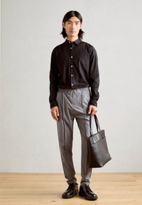 Schwarze Button-Down-Hemden, graue gestreifte Hosen, schwarze Ledertasche und schwarze Schnürschuhe. Glatter Stoff, lockere Passform und sichtbare Nähte.