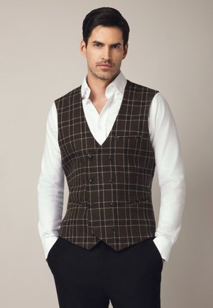 Brązowa kamizelka w kratę z podwójnym zapięciem, klapami z wycięciem i jedną kieszenią na piersi, noszona na białej koszuli z czarnymi spodniami.