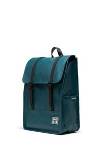 Teal backpack with a glossy finish, black straps, and flap closure. Features a front pocket and a logo label on the lower front.