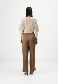Beige strikkegenser med løs passform, kombinert med brune høyt midje bukser, som har baklommer og glatt tekstur. Enkle design detaljer.