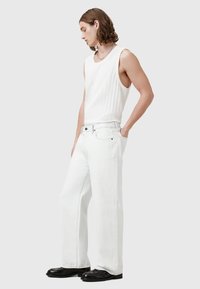 Hvid ribbet tanktop og løstsiddende hvide jeans med klassisk fem-lomme stil og sorte knapdetaljer. Modellen har sorte platformsko på.