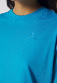 Tyrkysové bavlněné tričko s kulatým výstřihem, s malým vyšitým logem Jumpman na levé části hrudi. Hladká textury látky.