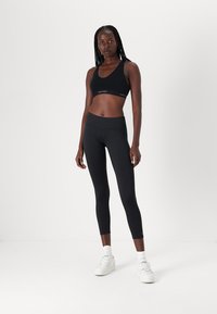 Schwarzer Sport-BH und hochgeschnittene Leggings aus einem glatten, dehnbaren Stoff. Das Outfit zeichnet sich durch minimale Markenkennzeichnung und eine taillierte Silhouette aus.