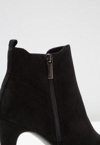 Czarne zamszowe botki za kostkę na wysokim obcasie z bocznym zamkiem błyskawicznym. Charakteryzują się gładką fakturą i przeszyciami na górnej krawędzi oraz przy zamku.