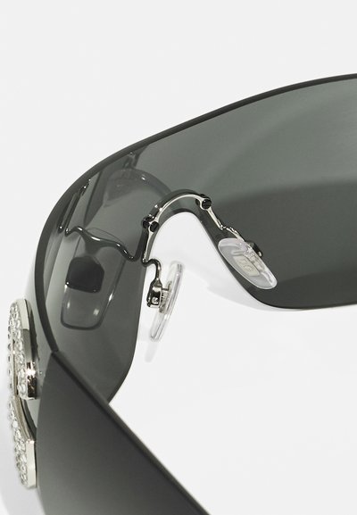 Sunglasses with dark gray lenses, metal frame, and clear nose pads. Features decorative silver accents on the sides. Smooth finish.