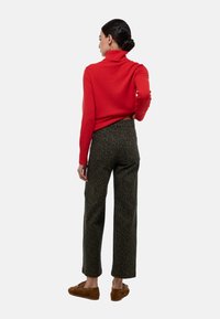 Un pull à col roulé rouge associé à un pantalon à motifs verts. La tenue présente une coupe décontractée et est portée avec des chaussures à enfiler marron.